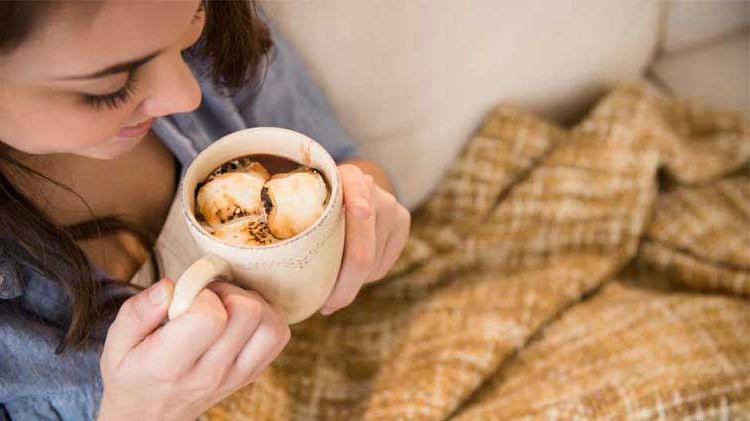 A woman enjoys her hot chocolate while covering up with an electric blanket.