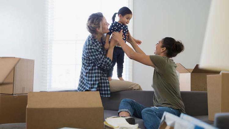 Two women and a little girl playing in a room full of moving boxes.